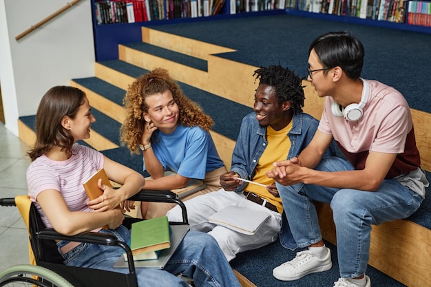 Gruppo eterogeneo di giovani che discutono di lavoro nella biblioteca del college, inclusa una studentessa con disabilità