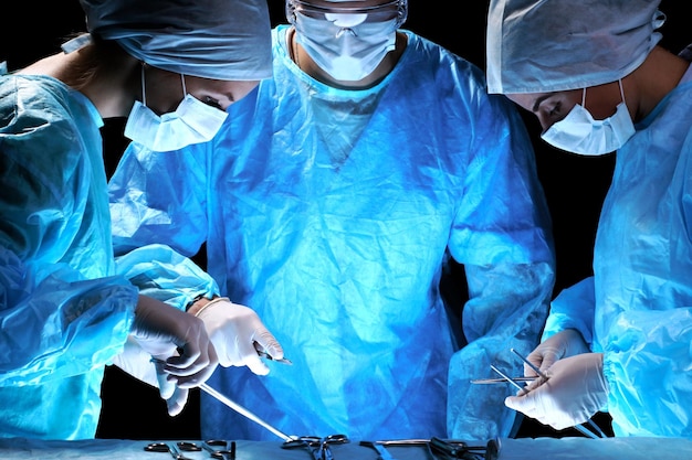 Gruppo medico che esegue l'operazione Gruppo di chirurgo al lavoro in sala operatoria in tonalità blu