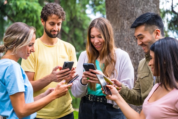 Gruppo multietnico con telefoni che guardano internet o social network nel concetto di tecnologia del parco