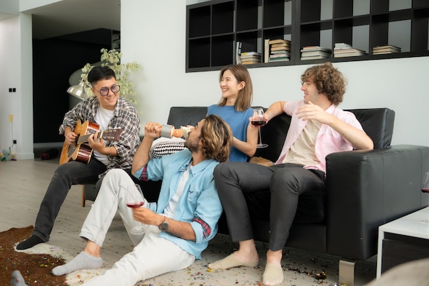 Gruppo multietnico di amici che si divertono a suonare la chitarra e cantare insieme a casa