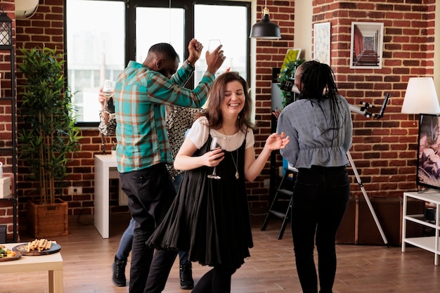 Gruppo multietnico di amici chiusi che ballano insieme in soggiorno alla festa del vino divertendosi. Giovani adulti che si godono la musica da discoteca a casa mentre celebrano l'anniversario dell'amicizia.