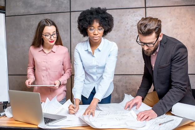 Gruppo multietnico di architetti o designer che lavorano insieme sui piani architettonici in ufficio