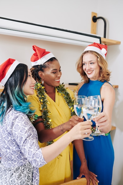 Gruppo multietnico di belle giovani amiche che celebrano il Natale e brindano con flauti di champagne