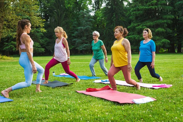 Gruppo multietnico di donne anziane che si allenano al parco con istruttore di fitness - Anziani attivi che fanno sport nella natura