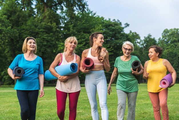 Gruppo multietnico di donne anziane che si allenano al parco con istruttore di fitness - Anziani attivi che fanno sport nella natura