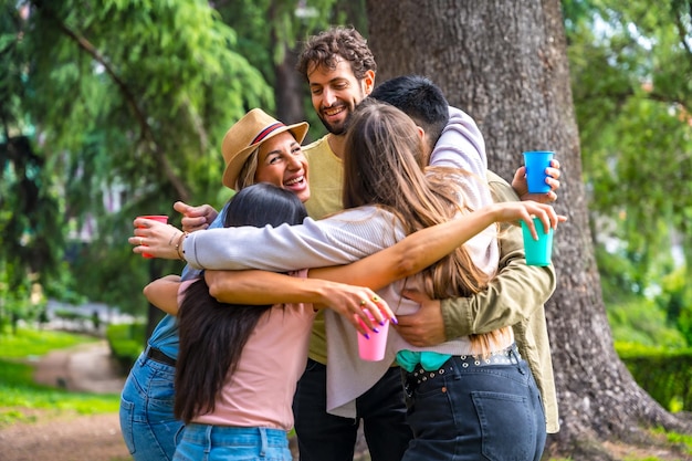 Gruppo multietnico di festa di compleanno nel parco cittadino abbracciato in un simbolo di amicizia per sempre