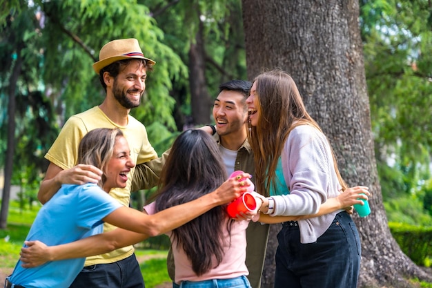 Gruppo multietnico di festa di compleanno nel parco cittadino che si abbraccia in un simbolo di amicizia per sempre e sorride molto