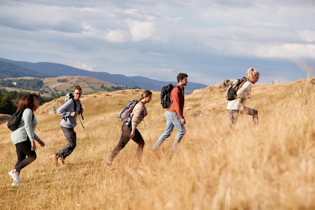 Gruppo multietnico di giovani amici adulti felici che scalano una collina durante una vista laterale di un'escursione in montagna