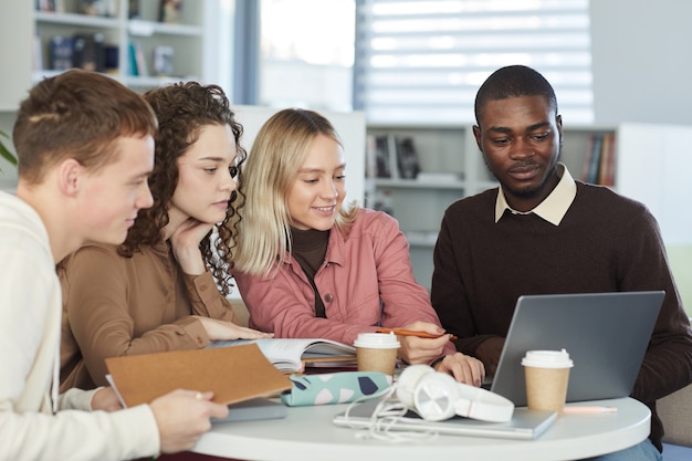 Gruppo multietnico di giovani che studiano insieme seduti a tavola nella biblioteca del college e guardando lo schermo del laptop