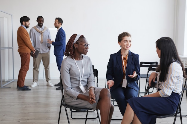 Gruppo multietnico di giovani donne che discutono di lavoro seduti in cerchio nella sala conferenze, copia spazio