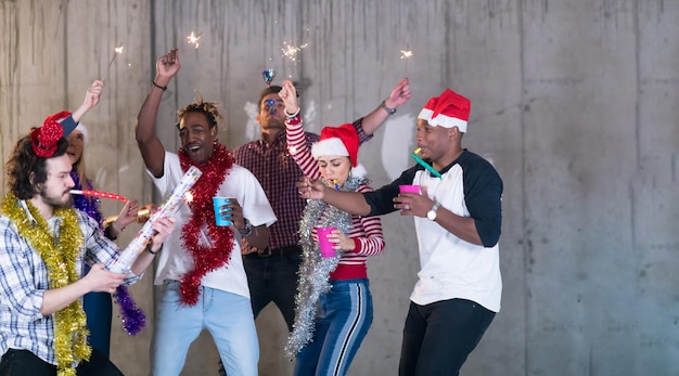 gruppo multietnico di giovani uomini d'affari casuali felici che ballano con le stelle filanti e si divertono mentre festeggiano il capodanno davanti al muro di cemento nel nuovo ufficio di avvio