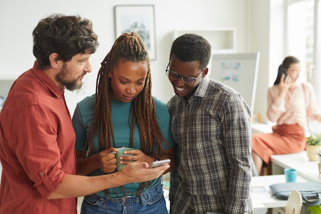 gruppo multietnico di persone che guardano lo schermo dello smartphone mentre si trovava in ufficio