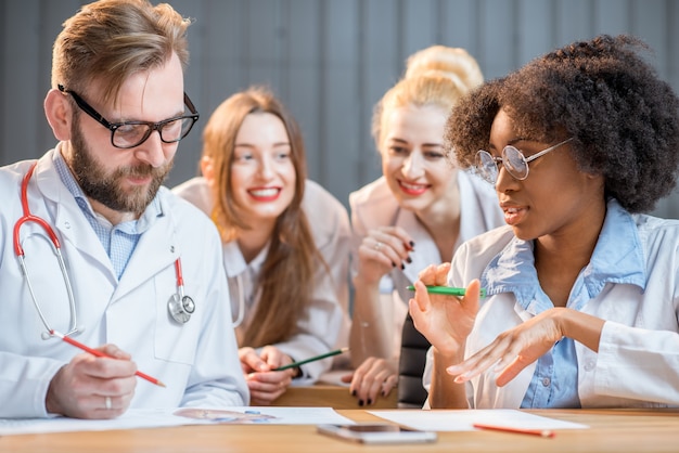 Gruppo multietnico di studenti di medicina in uniforme che discutono seduti insieme nell'aula moderna