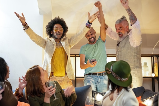 Gruppo multietnico di uomini che fanno il tifo per qualcosa guardando lo smartphone mentre un gruppo di donne stupite li guardano festa di celebrazione e concetto di sport