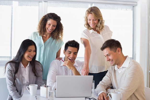 Gruppo sorridente casuale di affari che ha una riunione facendo uso del computer portatile