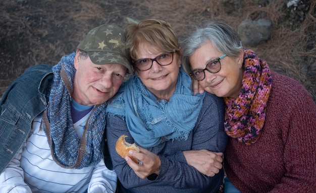 Gruppo sorridente di amici che si godono il loro picnic all'aperto mangiando un panino e guardando la fotocamera