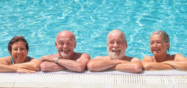 Gruppo sorridente di anziani adulti appoggiati al bordo della piscina che si godono le vacanze
