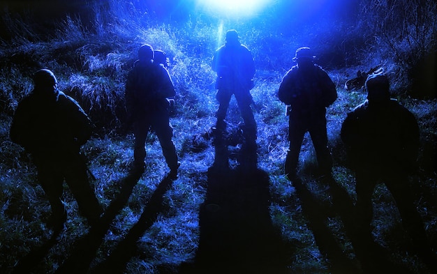 Gruppo tattico per le operazioni speciali dell'esercito, combattenti armati della squadra di sabotatori militari in piedi in un'area erbosa di notte, nascondendo i volti dietro le maschere, muovendosi silenziosamente nell'oscurità, pattugliando l'area di notte