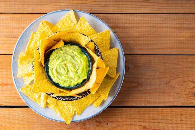 Guacamole con tortilla chips su tavole di legno. Patatine di nachos e salsa guacamole messicana su un piatto. Copia spazio. Vista dall'alto