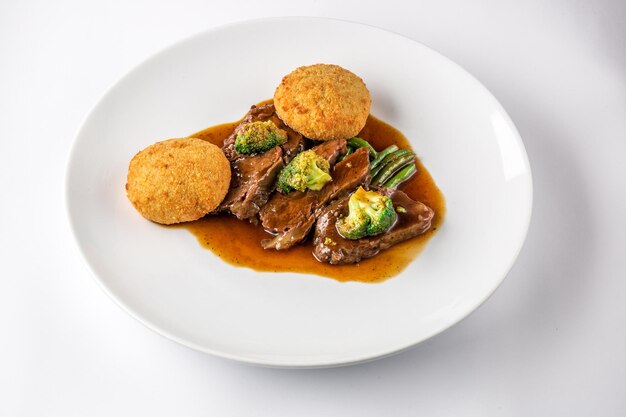 Guancia di manzo in salsa con broccoli e fagiolini su un piatto bianco