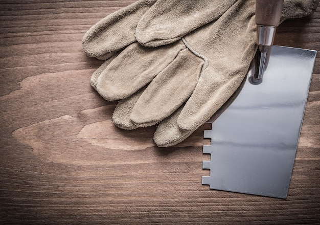 Guanti da lavoro e spatola di mastice su tavola di legno.