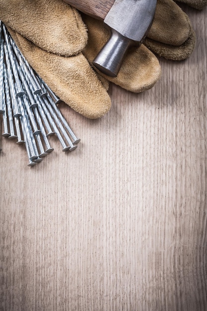 Guanti di sicurezza in pelle martello da carpentiere e pila di chiodi in acciaio inox su fondo in legno concetto di costruzione