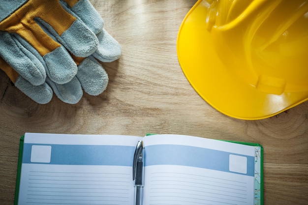 Guanti di sicurezza per casco da costruzione con penna per notebook aperti su tavola di legno.