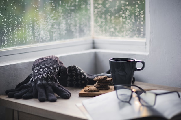 Guanti invernali e berretto con una tazza di caffè e un biscotto su un tavolo di legno per sfondo invernale