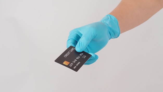 Guanto medico blu di usura della mano che tiene carta di credito nera su fondo bianco.