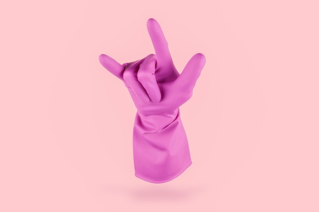 Guanto per la pulizia rosa che fa il gesto della roccia metallica con le dita su uno sfondo rosa