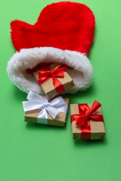 Guanto rosso della composizione di Natale del Babbo Natale con i regali su una priorità bassa verde. Modello per cartoline, imballaggio. Foto verticale.