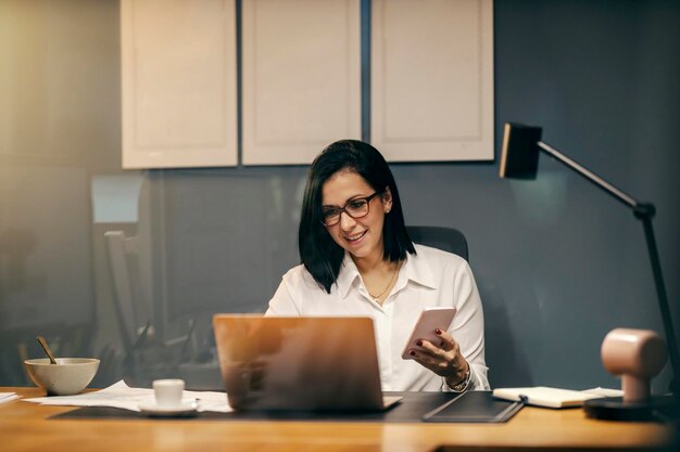 Guarda attraverso il vetro di una donna d'affari seduta in ufficio usando tecnologie all'avanguardia