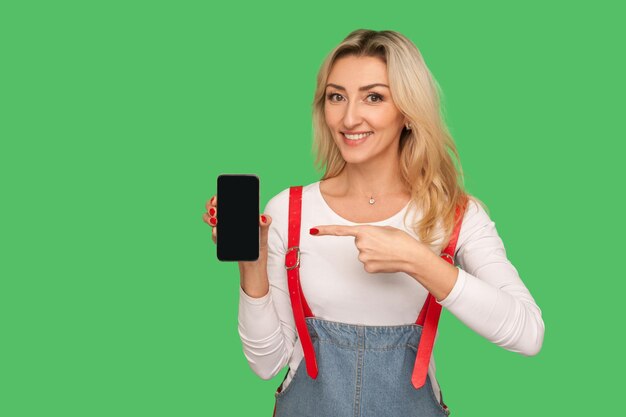 Guarda la fantastica app del cellulare Ritratto di donna adulta felice che punta allo smartphone con spazio per la copia del display mock up per l'applicazione pubblicitaria o il sito web girato in studio isolato su sfondo verde