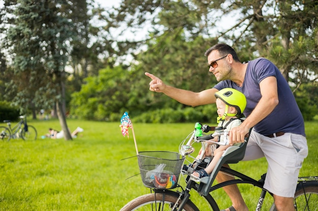 Guarda la giornata di famiglia attiva nella natura padre e figlio vanno in bicicletta attraverso il parco cittadino durante la soleggiata estate