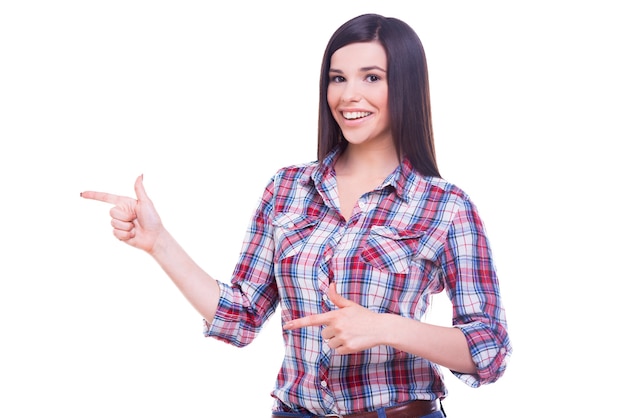 Guarda questo! Felice giovane donna sorridente che indica lo spazio della copia mentre sta in piedi isolato su bianco