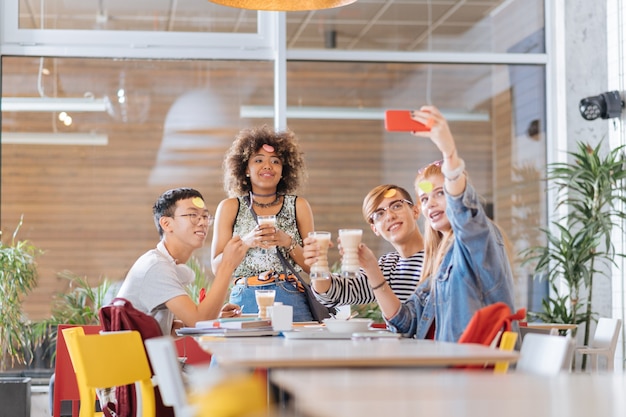 Guarda qui. Adolescenti felici che esprimono positività mentre fanno foto selfie