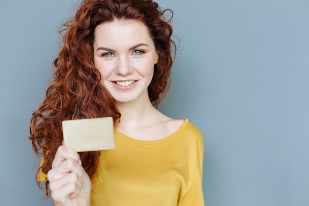 Guarda qui. Bella donna felice allegra che sorride e che ti guarda mentre ti mostra la sua carta