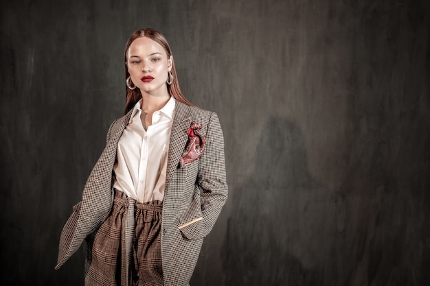 Guardami. Modello di moda professionale che dimostra cappotto elegante, in piedi sopra il muro grigio