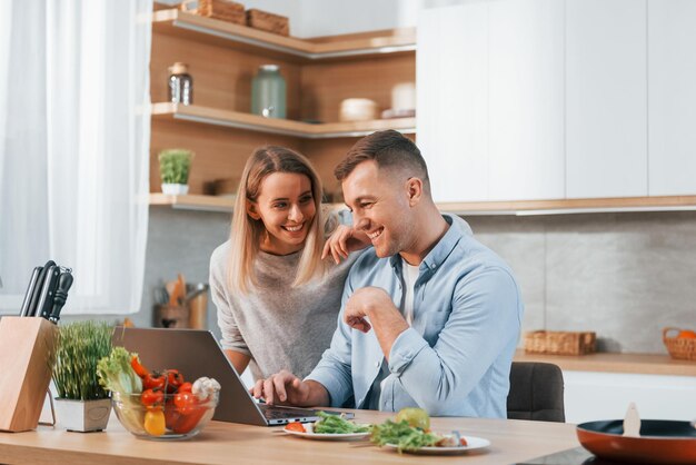 Guardando il computer portatile Coppia che prepara il cibo a casa sulla cucina moderna