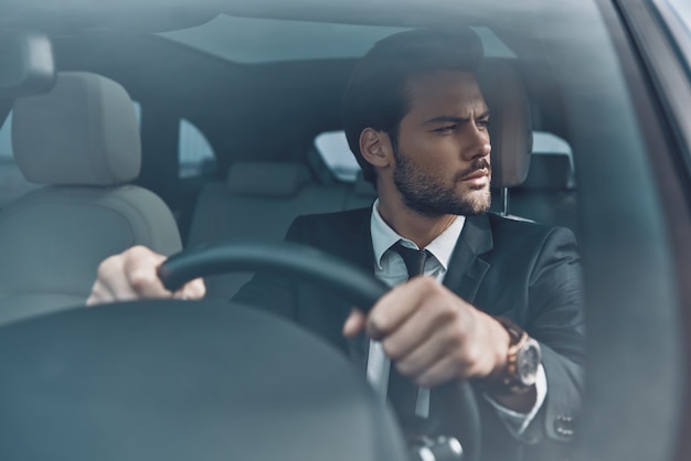 Guardando intorno. Bel giovane in completo che guarda lontano mentre guida un'auto