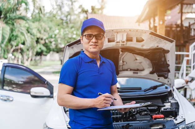 Guardando la fotocamera Meccanico asiatico dell'automobile che controlla la condizione della parte rotta del danno dell'auto diagnostica e ripara il veicolo al garage automobilistico