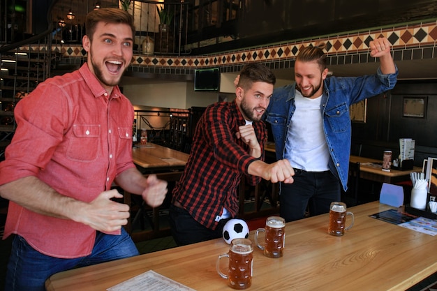 Guardare il calcio al bar. Amici felici che bevono birra e fanno il tifo per la squadra del cuore, celebrando la vittoria.