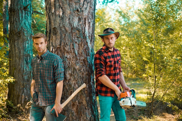 Guardie forestali nella foresta. Hipsters sulla faccia seria porta l'ascia. Il boscaiolo brutale tiene l'ascia. Concetto brutale del boscaiolo.