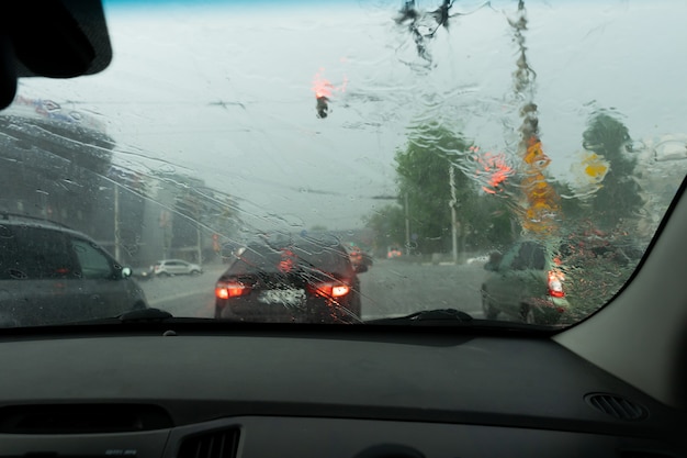 Guidare l'auto sotto la pioggia su strada bagnata. Tempo piovoso attraverso il finestrino dell'auto. Pioggia attraverso il parabrezza dell'auto in movimento. Vista attraverso il finestrino dell'auto sotto la pioggia. Tergicristalli dell'auto accesi sotto la pioggia.