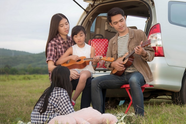 guidare nella famiglia delle vacanze; la famiglia asiatica è felice seduta nel bagagliaio aperto di un&#39;auto