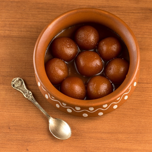 Gulab Jamun in una pentola di terracotta con cucchiaio e frutta secca. Dessert indiano o piatto dolce