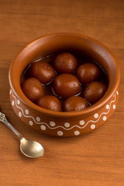 Gulab Jamun in una pentola di terracotta con cucchiaio e frutta secca. Dessert indiano o piatto dolce