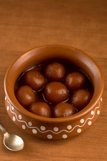 Gulab Jamun in una pentola di terracotta con cucchiaio e frutta secca. Dessert indiano o piatto dolce