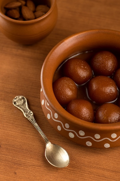 Gulab Jamun in una pentola di terracotta con cucchiaio e frutta secca. Dessert indiano o piatto dolce