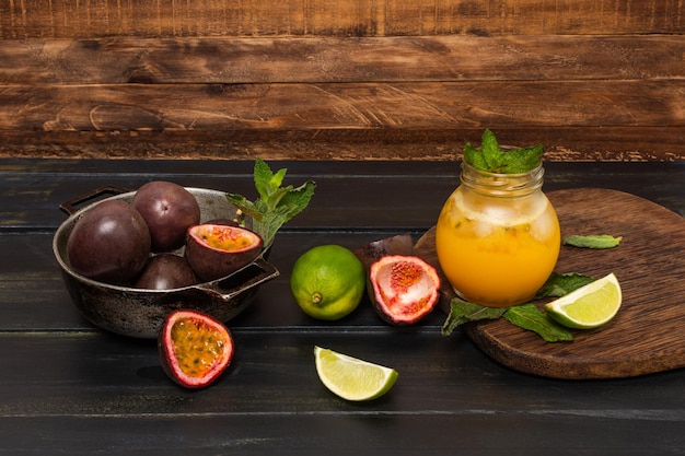 Gulupa o succo di frutto della passione circondato da bucce e frutti interi e tagliati limoni e menta verde su un fondo di legno invecchiato